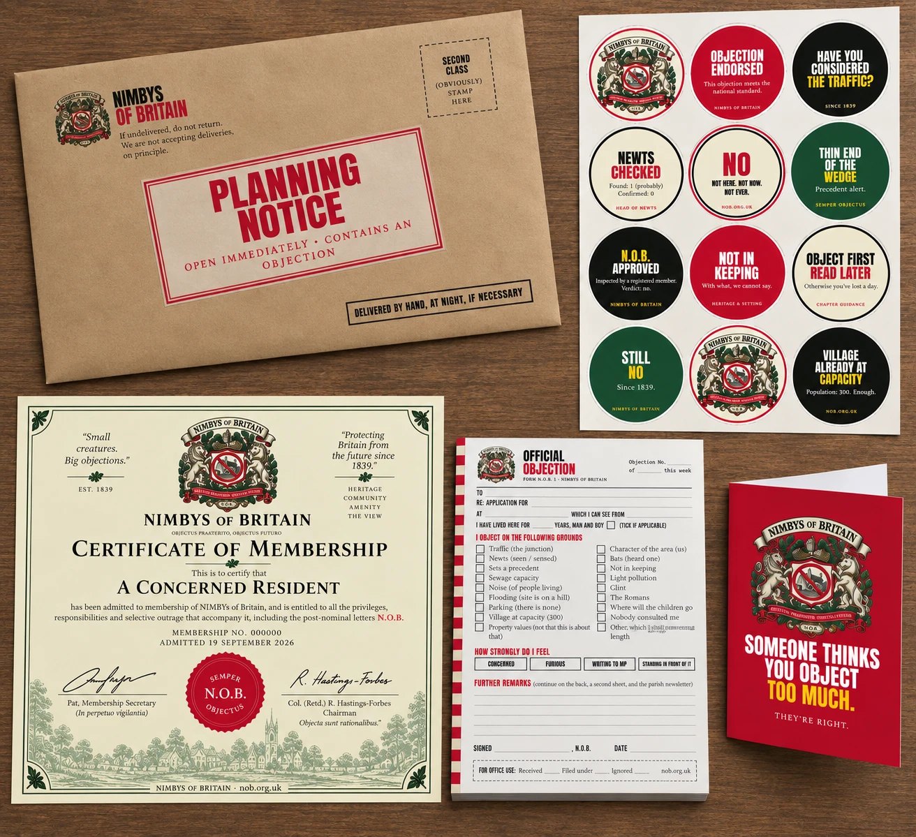The gift pack laid out on a wooden table: a manila envelope stamped PLANNING NOTICE, the A4 sticker sheet, the Certificate of Membership, the Official Objection pad and the red gift card reading Someone Thinks You Object Too Much