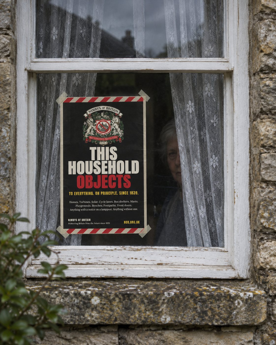 The black This Household Objects poster taped inside a cottage sash window, net curtains parted, an elderly woman watching from behind them.