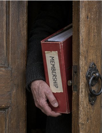 Only a hand is visible, holding a fat ring binder through a partly opened door. The rest of the person is in shadow.